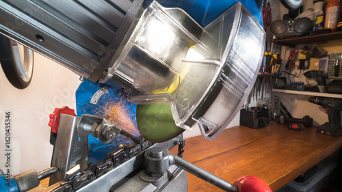 Electric saw chain grinder at sharpening cutting edge of steel tooth on workbench in workroom. Closeup of rotating disc sharp blade with transparent protective cover at grinding by chainsaw sharpener.