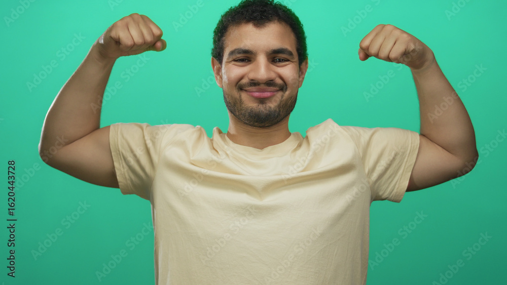 Fototapeta premium Young hispanic man flexing bare forearms and clenched fists in a bright green studio space; confidence motivation empowerment resilience.
