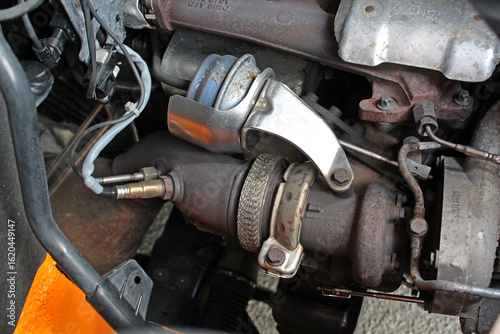 Diesel engine turbine. Turbine vacuum actuator. Close-up turbocharger system in diesel engine bay, showing metal piping, clamps, sensors, and manifold with mechanical connections and heat shield wrap.