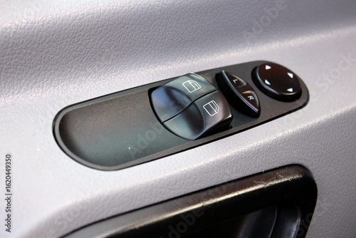 Car windows control. Car interior details of door handle. Close-up of a vehicle’s interior power window and mirror control panel with black plastic buttons, mounted on a light gray textured door panel