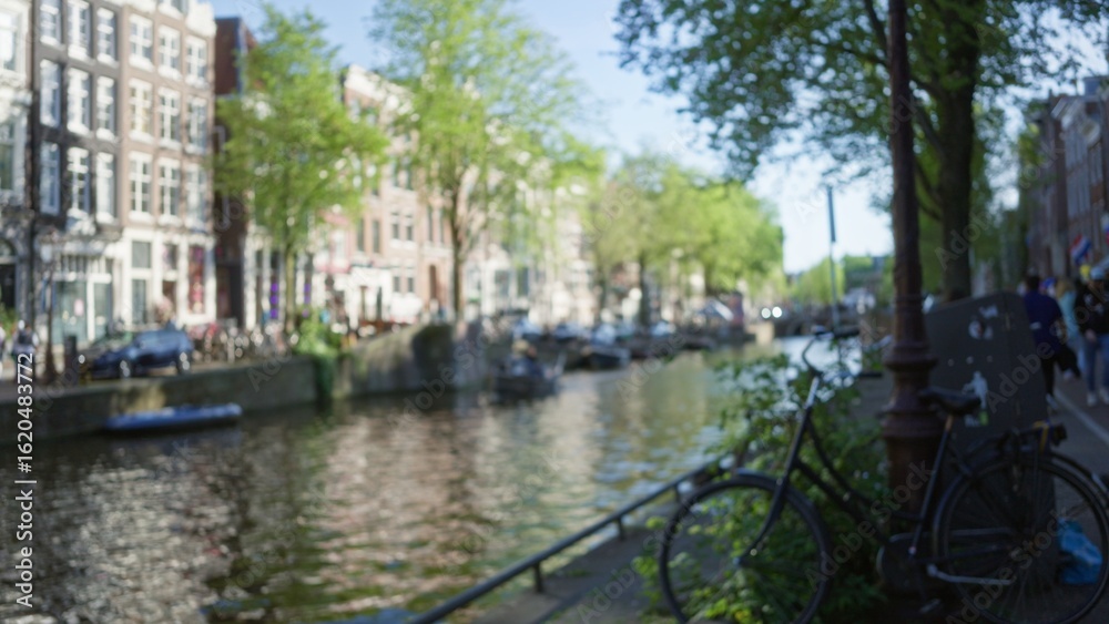 Fototapeta premium Blurred canals of amsterdam with defocused bicycles and lush greenery lining the waterways on a sunny day, capturing the essence of the netherlands' charming capital.