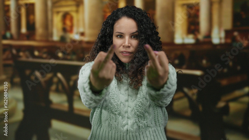 Wallpaper Mural Woman gesturing with defiance in a church setting, wearing a sweater and displaying a bold expression, capturing the contrast between her action and the serene environment. Torontodigital.ca