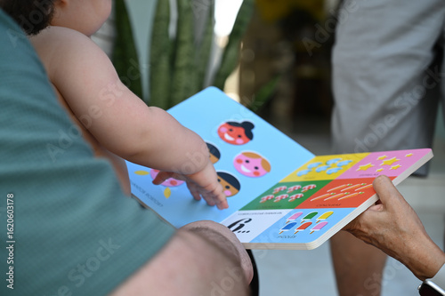 toddler pointing at pictures in baby book, early childhood learning through play, family interaction with educational board book, baby interacting with book


