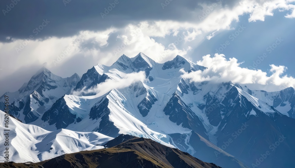 Obraz premium Majestic Snow-Capped Mountains Under Dramatic Clouds with Sunlight Breaking Through the Sky