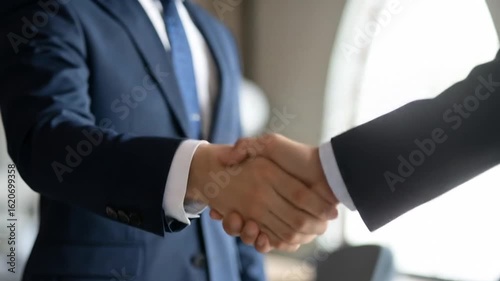Close Up of a Business Handshake Between Two Individuals in Dark Blue Suits in Office Setting