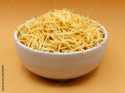 STRAW POTATOES IN A WHITE BOWL ON A YELLOWISH ORANGE BACKGROUND