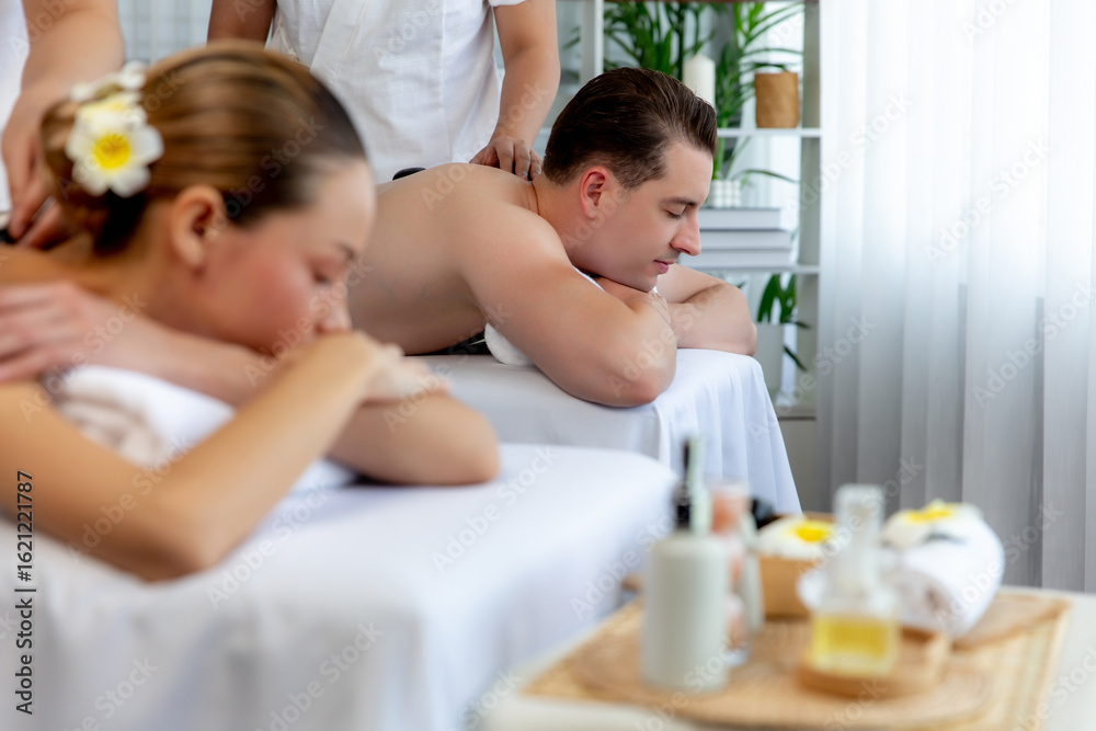 Fototapeta premium Hot stone massage at spa salon in luxury resort with day light serenity ambient, blissful couple customer enjoying spa basalt stone massage glide over body with soothing warmth. Quiescent