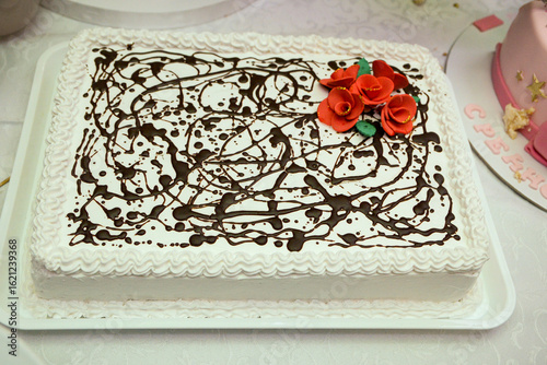 A white square cake decorated with whipped cream, edible edible roses with green petals and chocolate that looks like it has been sprinkled on the cake.