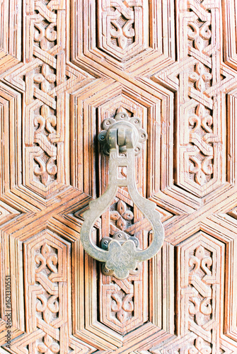 Bronze door knocker on textured, wooden door in Morocco