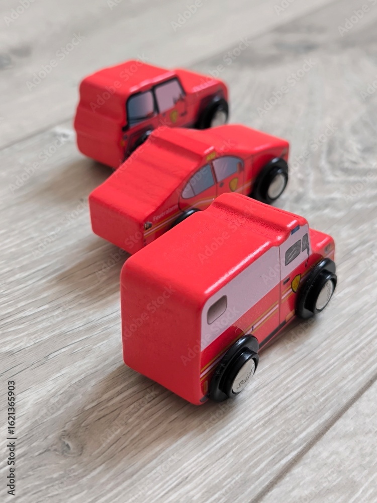 Obraz premium Red wooden toy cars on a light wooden floor.