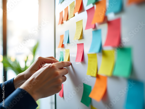 Hands placing a yellow sticky note on a board covered in colorful notes. A visual representation of brainstorming and project management.