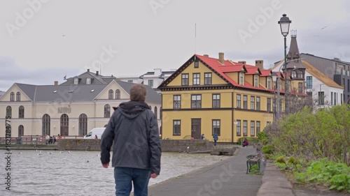 Man walks along Tjornin lake toward downtown Reykjavik on a cloudy day