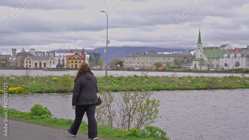 Woman walks along Tjornin lake in downtown Reykjavik on a cloudy day