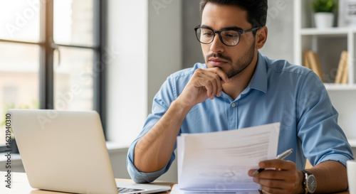 Focused Man Reading Documents with Glasses and Laptop.