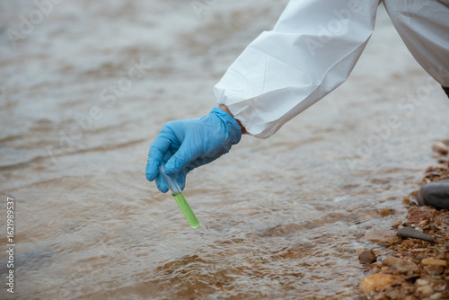 Scientist collects water sample from river for environmental testing during daytime