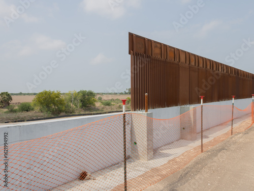 A focused photograph of a segment of the U.S.–Mexico border wall, emphasizing the vertical steel slats and the stark presence of the structure in the South Texas landscape.