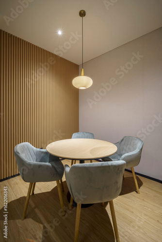 A cozy meeting nook in a modern office with four plush chairs, a round table, and a stylish pendant lamp against a fluted wood wall.