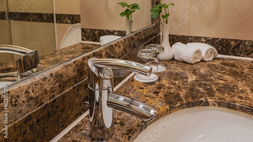 Fotografija A shiny stainless faucet on the edge of a white oval washbasin
