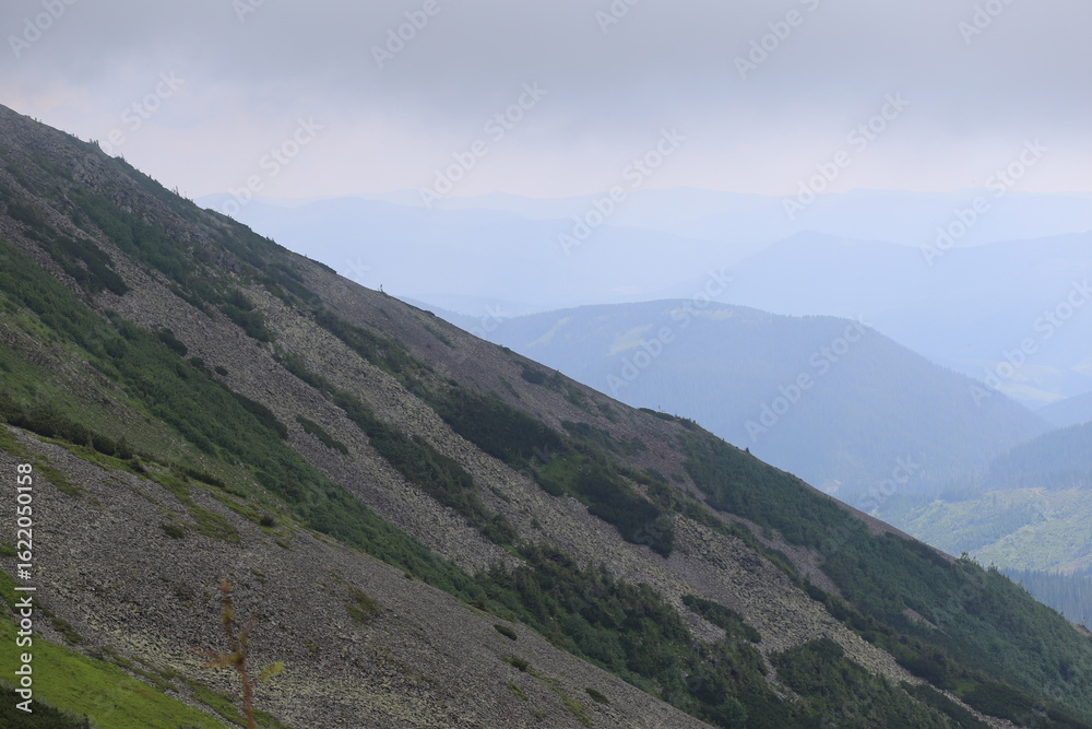 Fototapeta premium Tall Mountain Peaks with Green Slopes and Light Clouds
