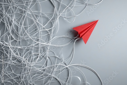 Bright red paper airplane navigates a chaotic web of swirling white strings on gray backdrop