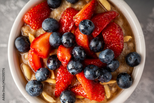 Oatmeal with ripe strawberries, blueberries and honey in the bowl. Selective focus. Shot from above.