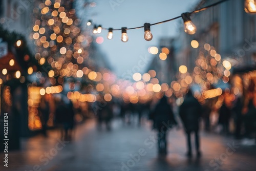 Fototapeta Naklejka Na Ścianę i Meble -  Blurred city street at night, festive lights strung overhead, people walking