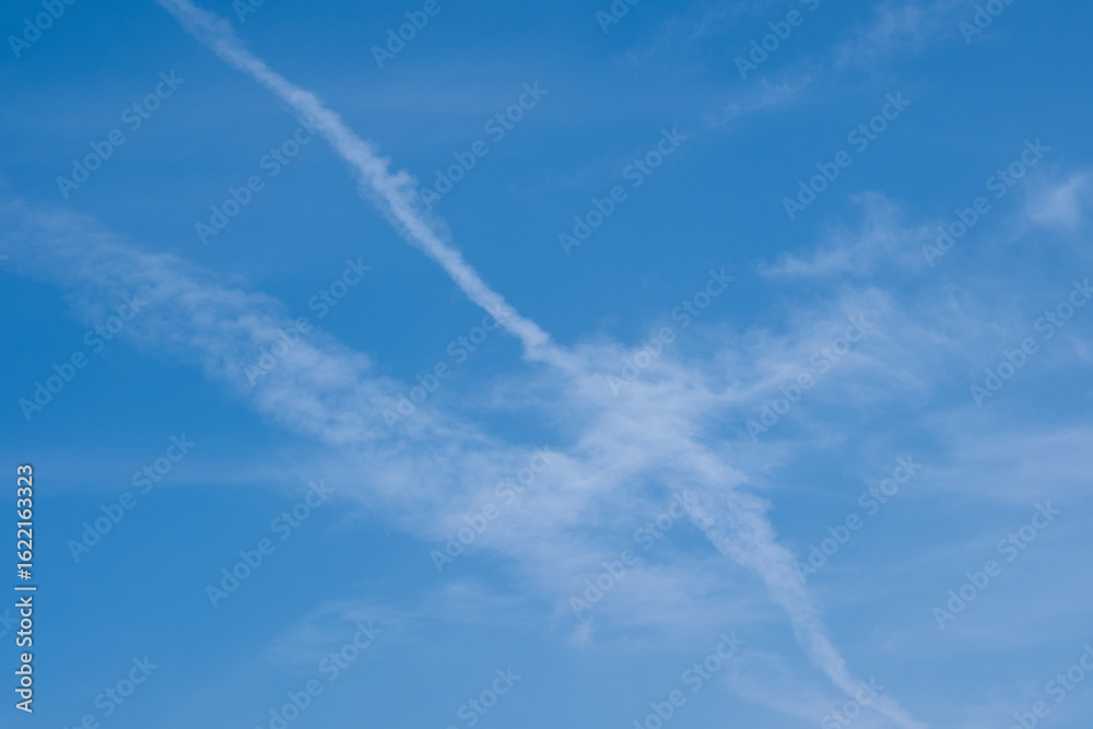 Blue sky with white clouds and wispy contrails creating patterns in the atmosphere on a sunny day, perfect for backgrounds or nature-themed projects Blue sky with white clouds and wispy contrails creating patterns in the atmosphere on a sunny day, perfect for backgrounds or nature-themed projects