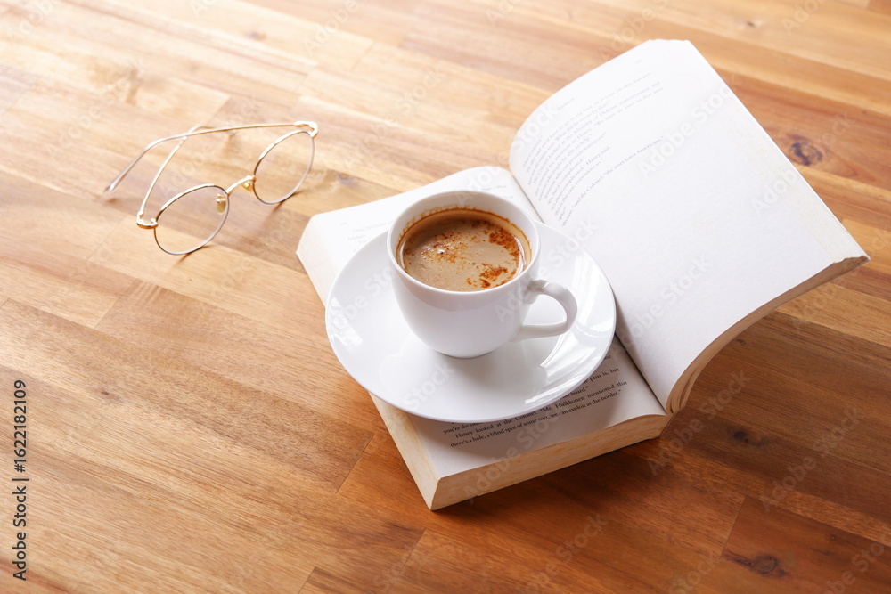 Obraz premium ページを開いたペーパーバック（洋書）とコーヒーの入ったコーヒーカップで、コーヒーを飲みながら読書を楽しんでいるイメージ 