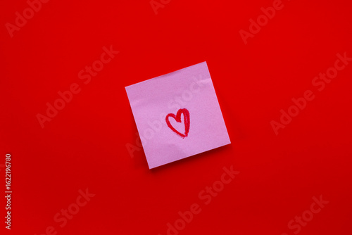 Fotografie Pink sticky note with red heart drawing on vibrant red background for love notes