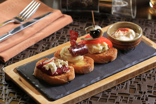 A close-up, three-quarter view shows a trio of gourmet tapas or bruschetta on toasted bread