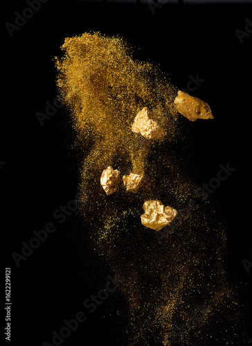 Explosion metallic gold glitter sparkle and gold nuggets on black background.