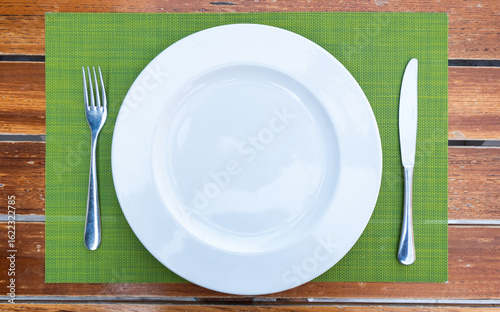 White ceramic plate and metal silverware including knife and fork on placemat on dining table