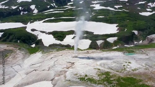 Aerial view of plumes of steam rising from geysers amid a landscape of snow and green vegetation, creating a striking contrast, Kamchatka Krai, Russia.