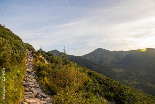 Mountain trail with sunrise view in Tatra Mountains, Zakopane, Poland.
Stone hiking path on green slope with mountain sunrise
