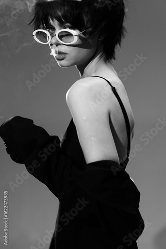 Schilderij op canvas Black and white portrait of a stylish woman wearing sunglasses with a bare shoulder and layered hair, creating a moody and fashionable look