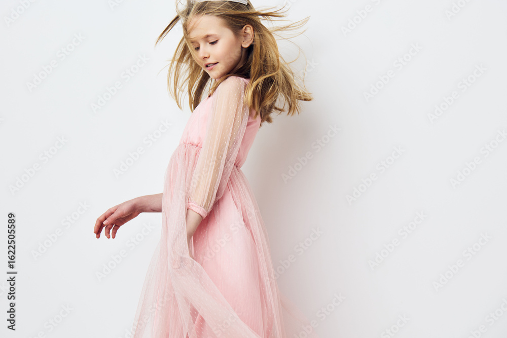 Naklejka premium Young girl in a pink tulle dress joyfully dancing against a white backdrop, embodying innocence and playfulness in a whimsical spring setting