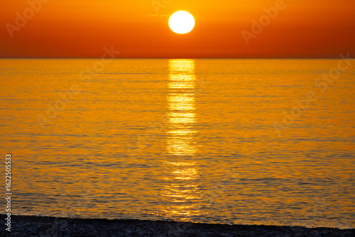 A bright orange sunset over the sea with a path on the water leading to the horizon