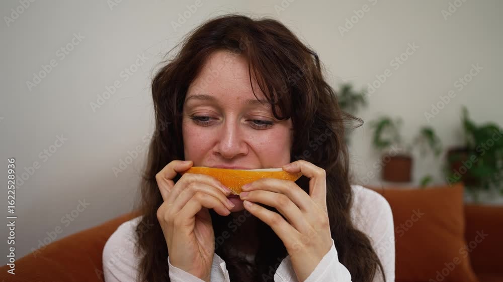 Young woman savoring ripe, juicy melon slice with pure enjoyment, experiencing moment of blissful pleasure while sitting comfortably on sofa Young woman savoring ripe, juicy melon slice with pure enjoyment, experiencing moment of blissful pleasure while sitting comfortably on sofa