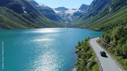 A car drives on a winding road beside a turquoise lake surrounded by mountains and glaciers
