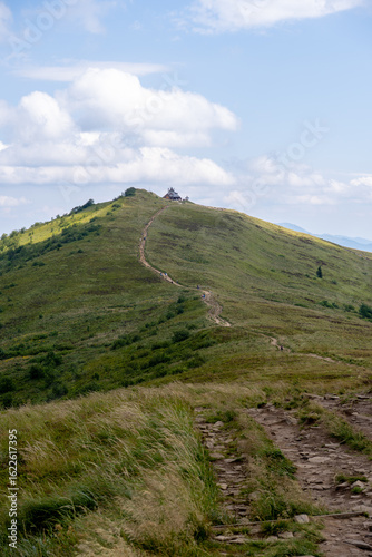 Fototapeta Naklejka Na Ścianę i Meble -  Mountain trail leading to the summit of Połonina Wetlińska with views of Bieszczady Mountains, Poland. Rocky path, green hills, and blue sky filled with clouds.