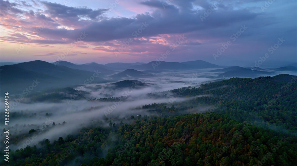 Fototapeta premium Morning fog rolling over dense green forested hills under cloudy sky