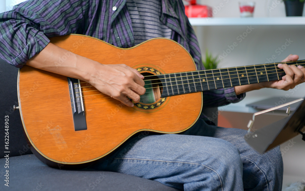 Fototapeta premium Young Asian man performing music in house with guitar. Creative enjoying music practice