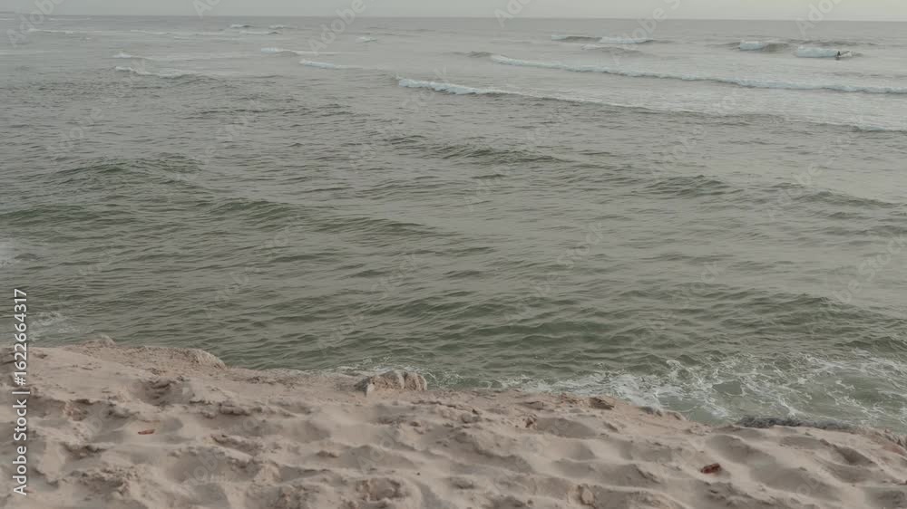 soft ocean waves roll onto sandy beach with subtle foam and overcast sky soft ocean waves roll onto sandy beach with subtle foam and overcast sky