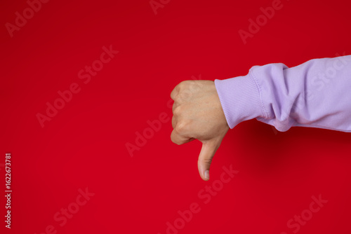 Male hand making thumbs down gesture on a red background, disapproval concept