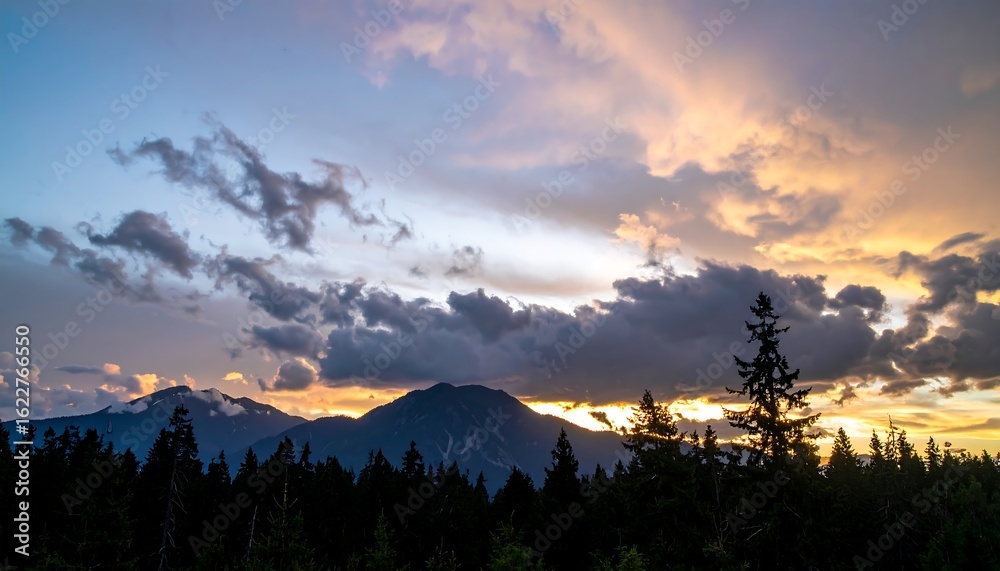 Fototapeta premium Colorful sunset sky over a mountain range and silhouetted forest.
