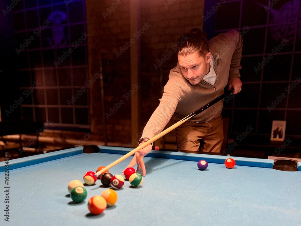 Fototapeta premium Brunette middle-age man holding arm on billiard table, playing snooker game or preparing aiming to shoot pool balls. sport game snooker billiards