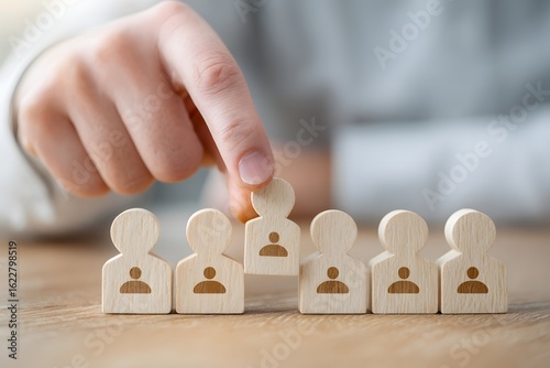 Hand selecting a wooden figure from a group representing recruitment and team selection