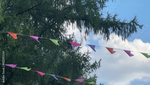Garlands of colorful cloth flags hang from the tree, fluttering the blue sky.
