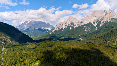 Fotografia Aerial view of scenic alpine valley with pine forest and rocky mountain range un