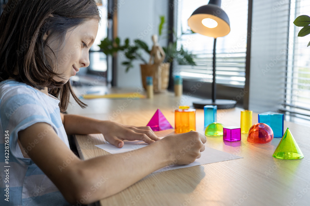 Teen girl studying geometric shapes at school desk, preparing for back to school season and exploring math concepts through colorful 3D figures during interactive learning activity in class. Teen girl studying geometric shapes at school desk, preparing for back to school season and exploring math concepts through colorful 3D figures during interactive learning activity in class.
